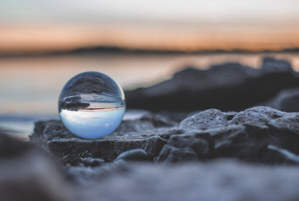 A crystal ball reflecting a serene sunset over rocks by the water, with a blurred background