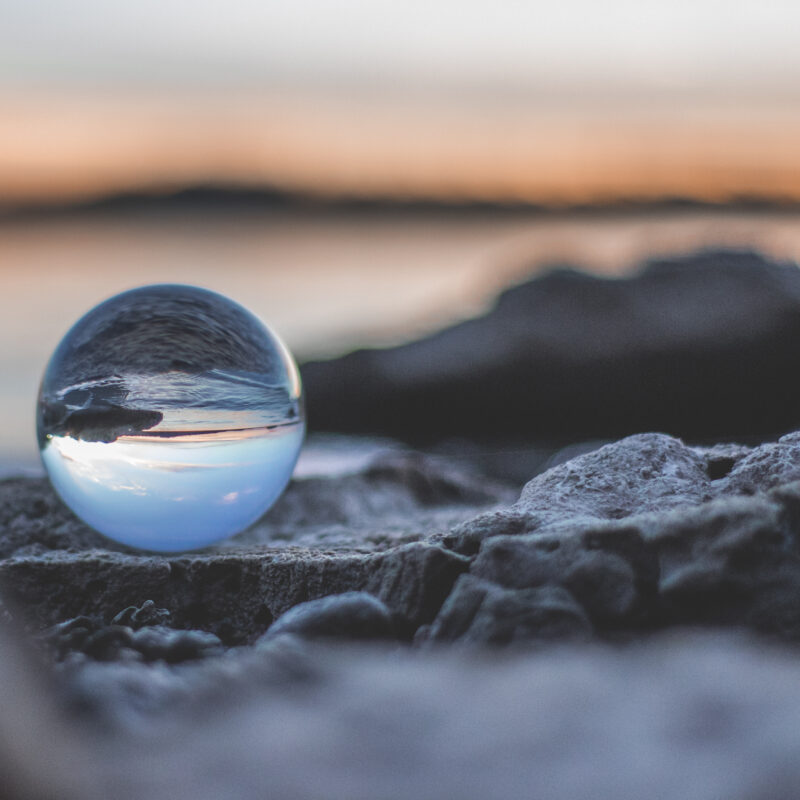 A crystal ball reflecting a serene sunset over rocks by the water, with a blurred background