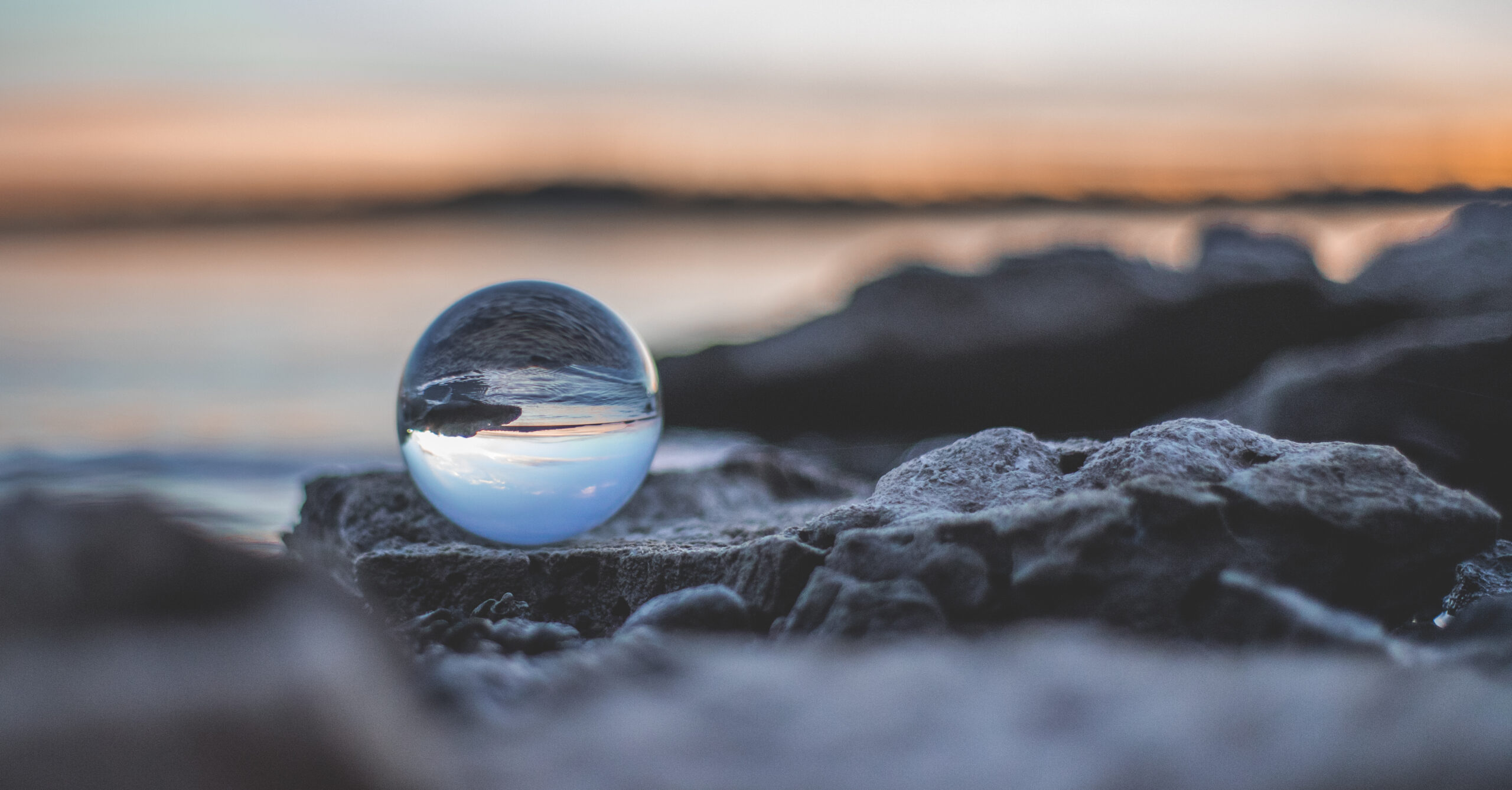 A crystal ball reflecting a serene sunset over rocks by the water, with a blurred background