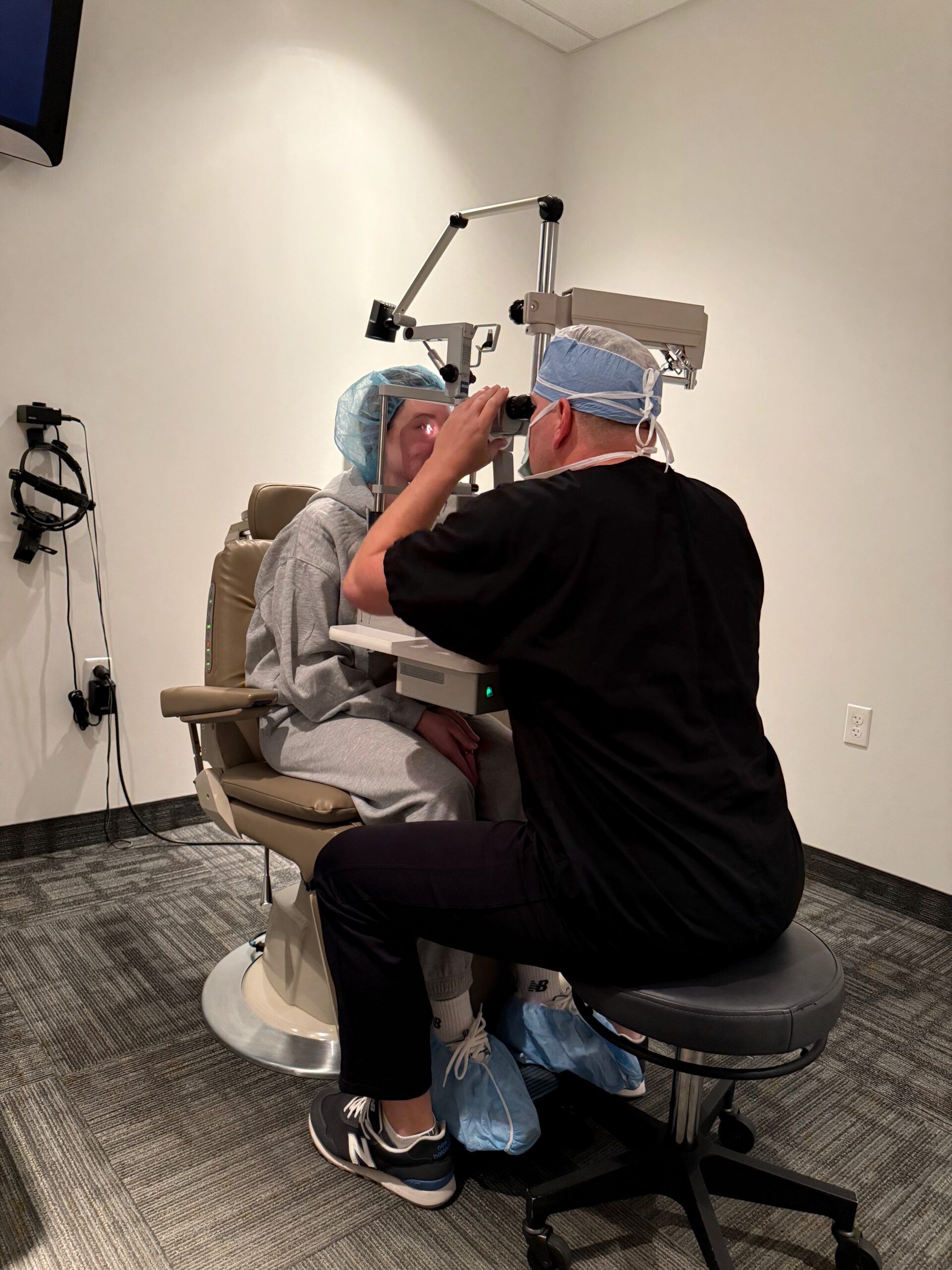 A Hoopes Vision surgeon examining a patient's eyes at a slit lamp during a consultation